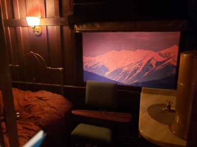 Photo of the inside of one of the cabins in the train exhibit. Shows a bed, chair, and sink with a view of a window.